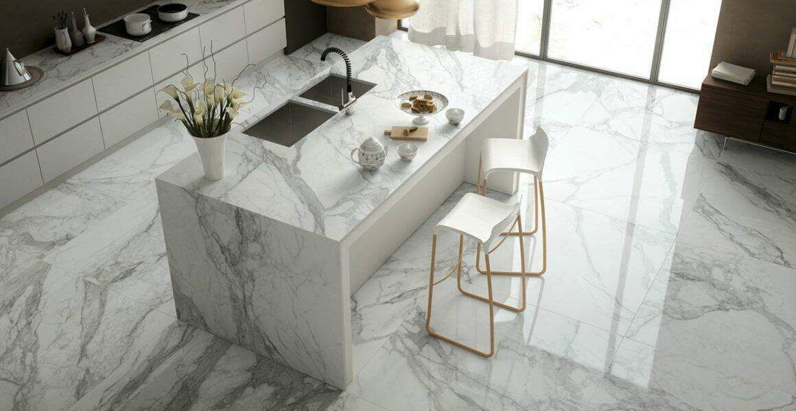 A kitchen with a marble counter top , sink , and stools.