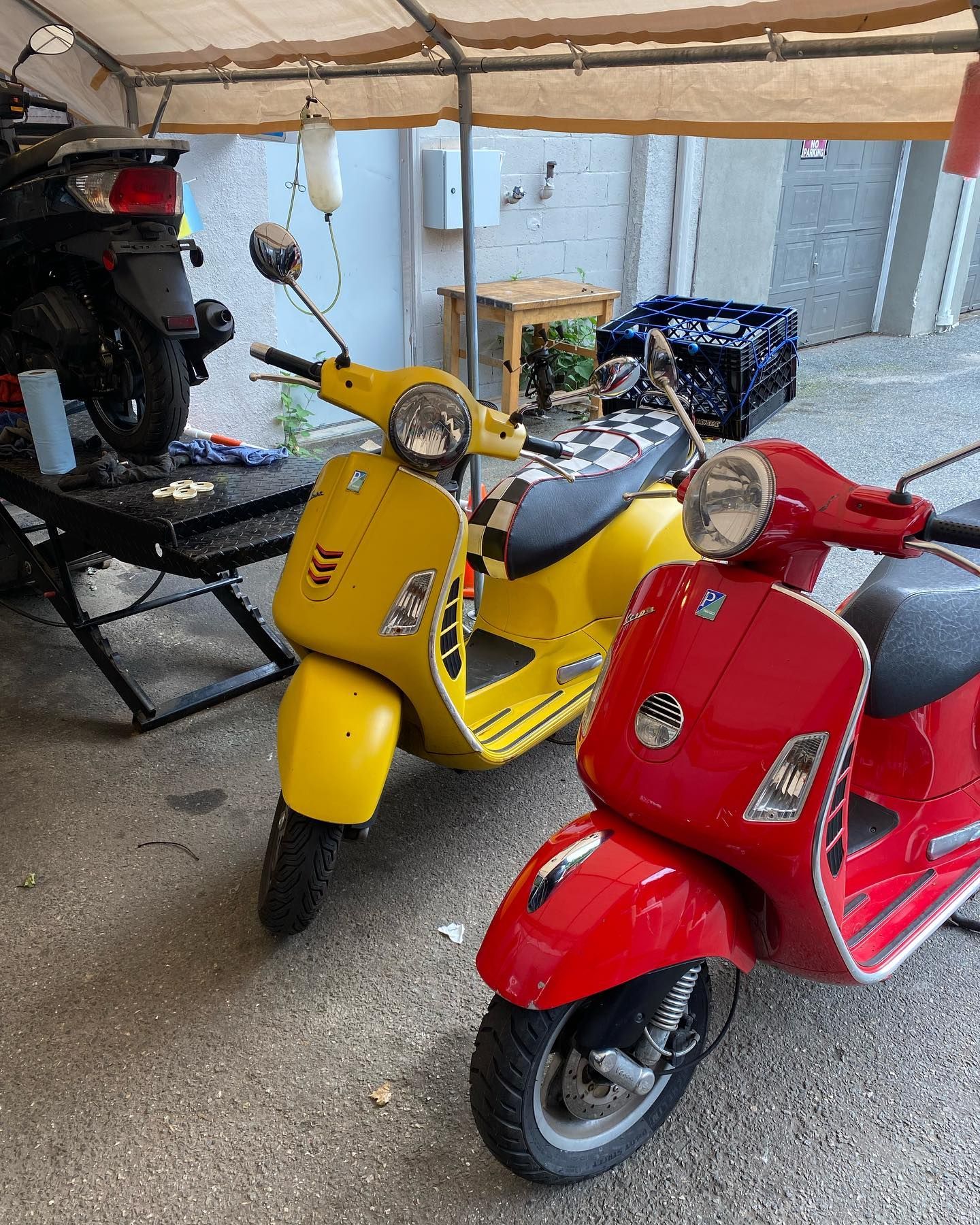 Yellow and red Vespa scooters parked under a canopy; a third scooter is on a lift in the background.