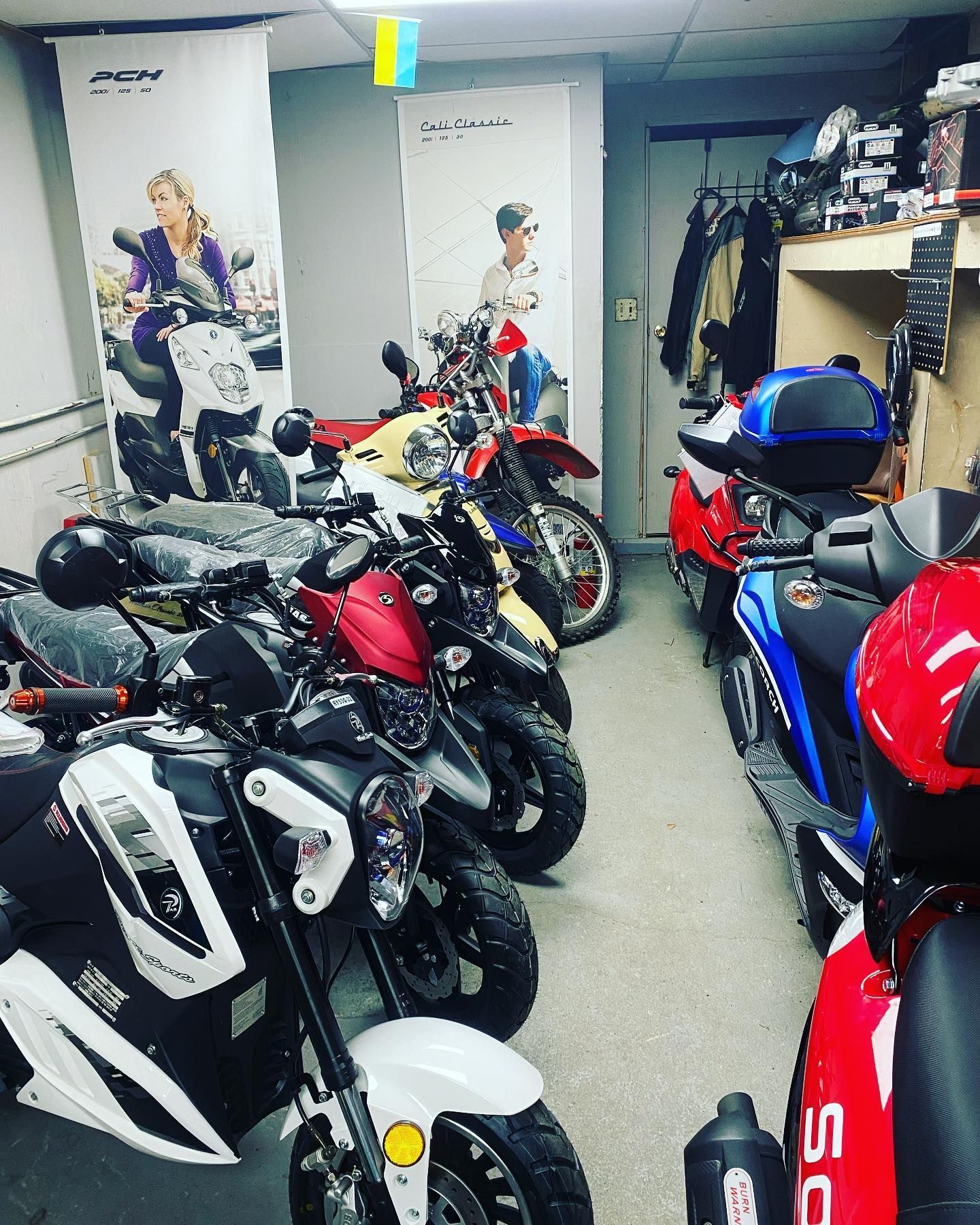Scooters in a showroom. Various colors and styles are on display, alongside advertising banners.