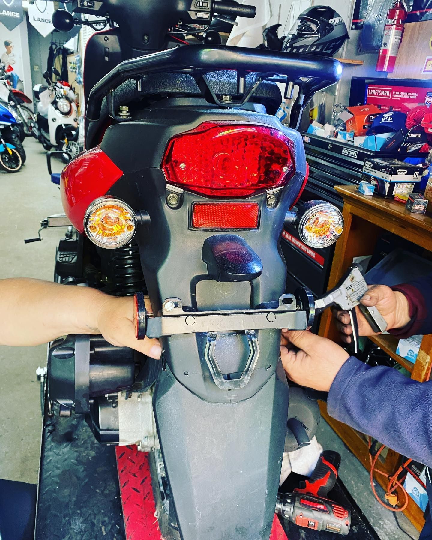 Two people working on the rear of a scooter, attaching a license plate holder.