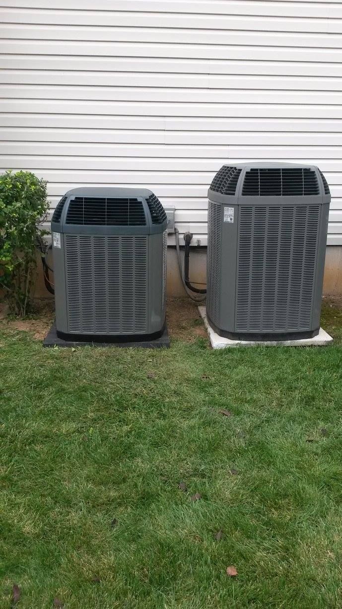 Two air conditioners are sitting on top of a lush green lawn in front of a house.