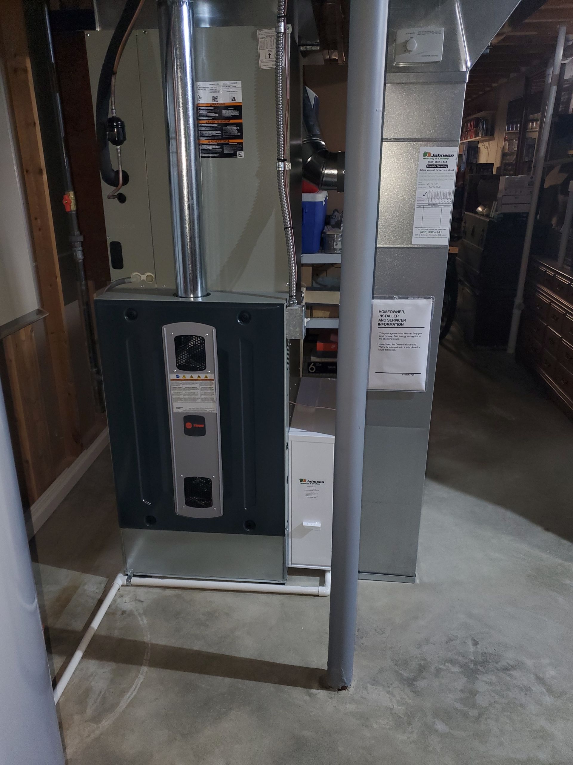 An air conditioner is sitting in a basement next to a pipe.