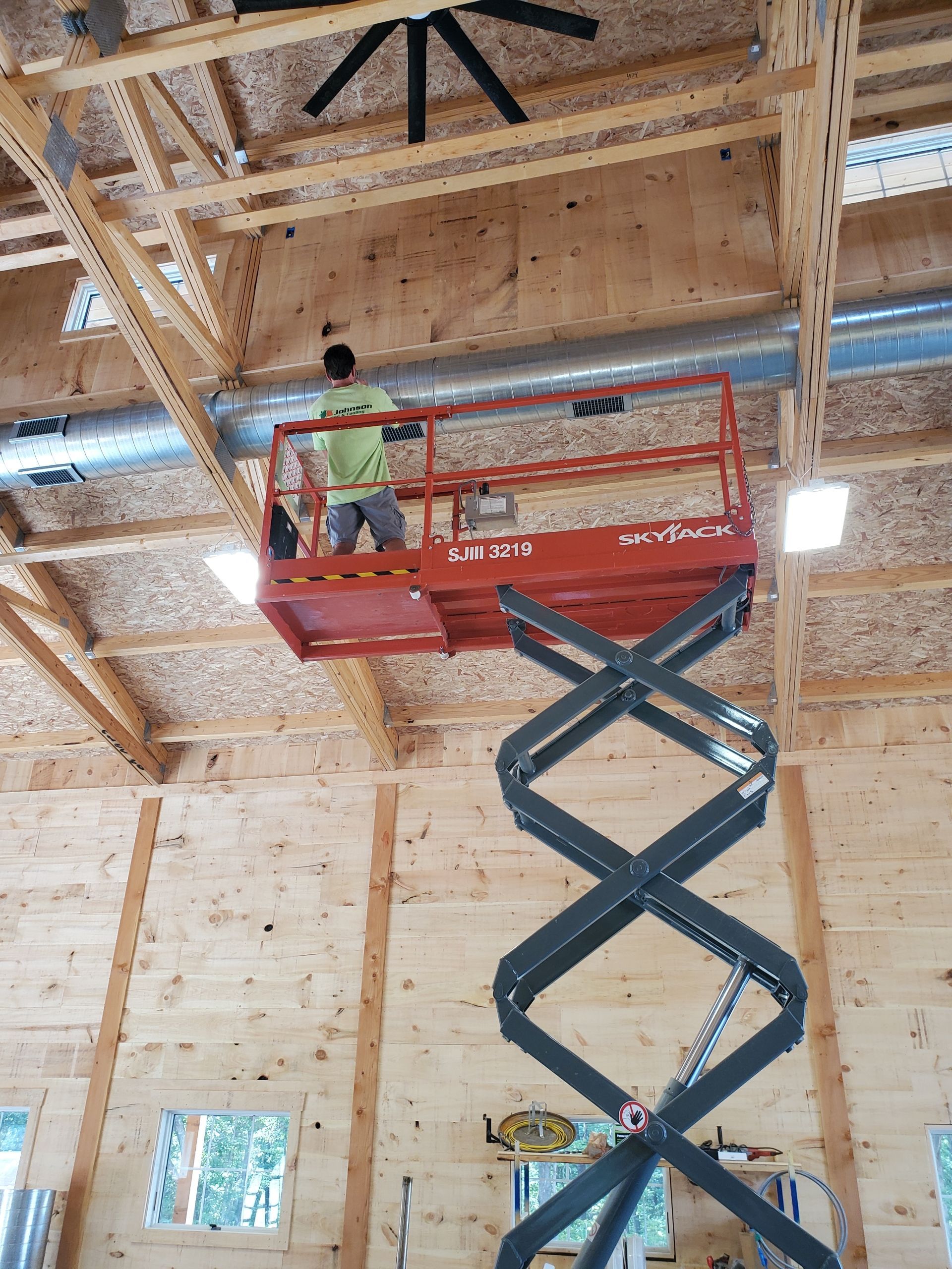 A man is standing on a scissor lift in a wooden building.