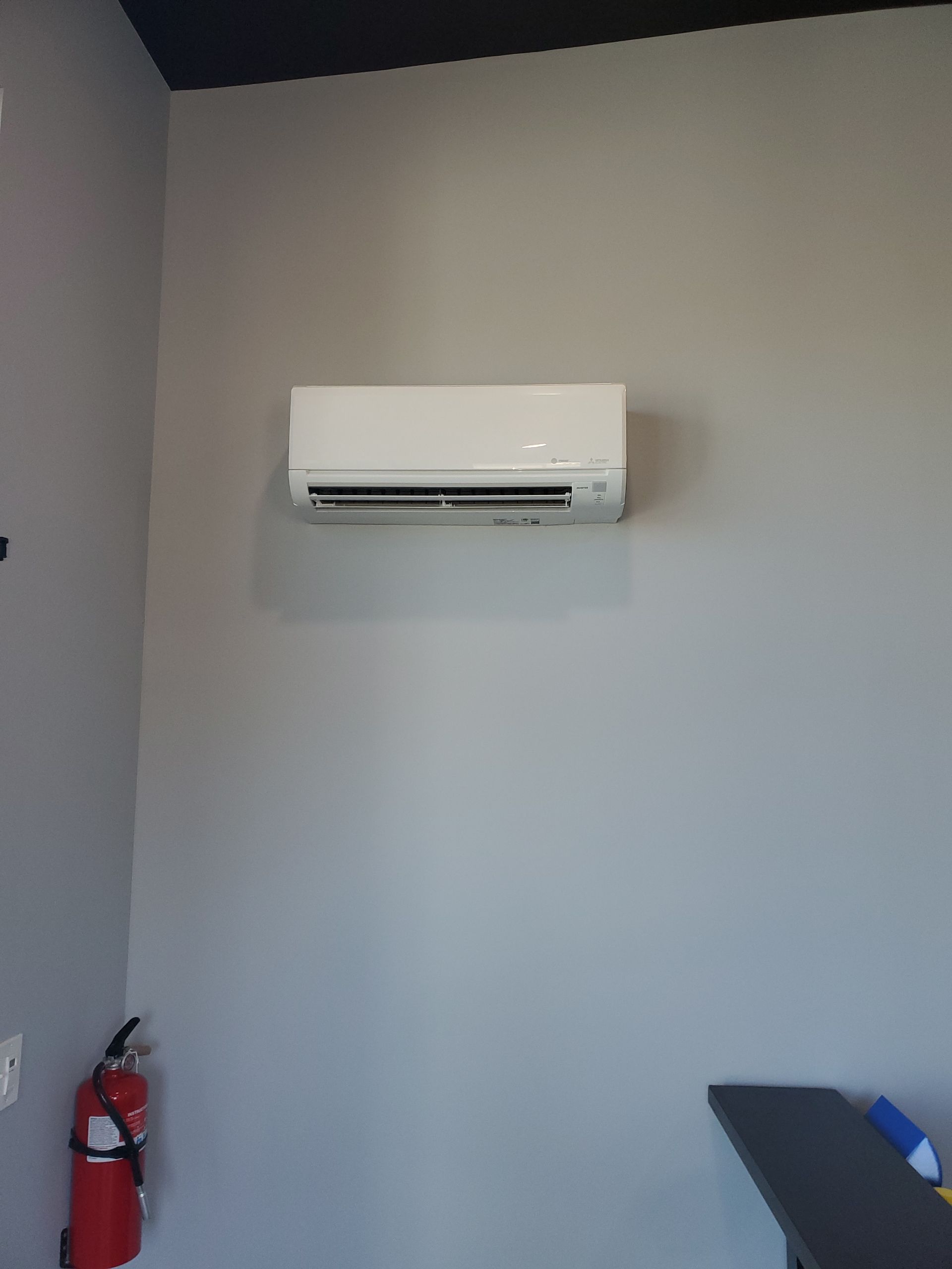 A room with a fire extinguisher and a wall mounted air conditioner. mini-split