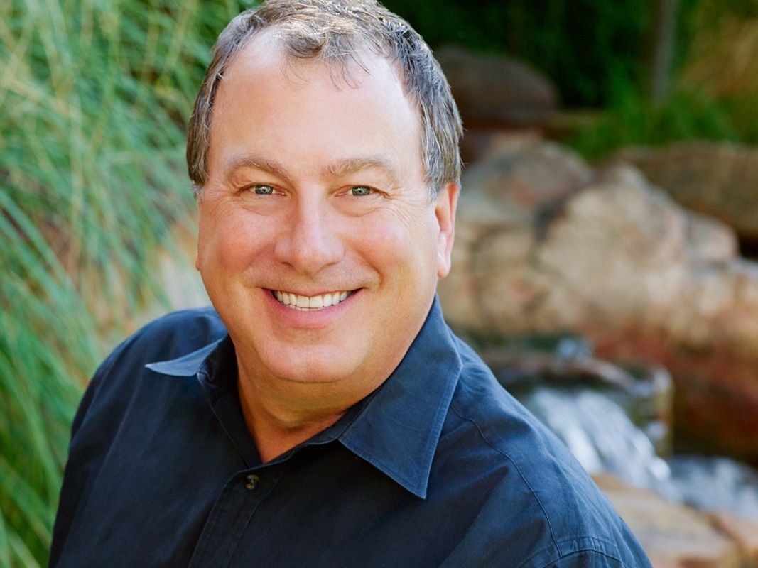 A man in a black shirt is smiling in front of a waterfall.