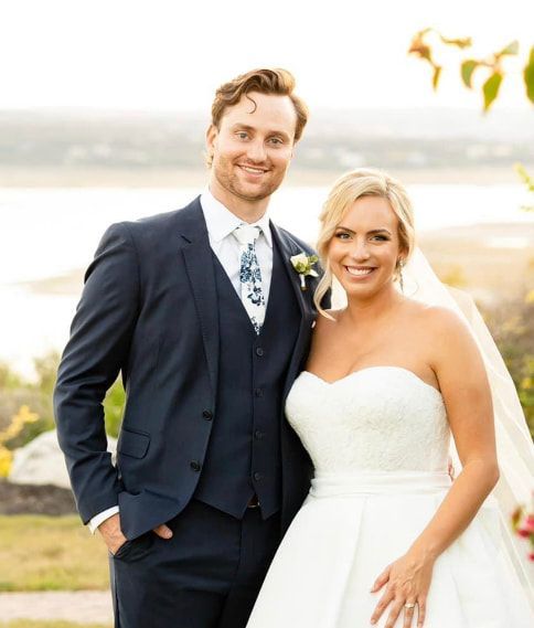 A bride and groom pose for a picture in front of a body of water