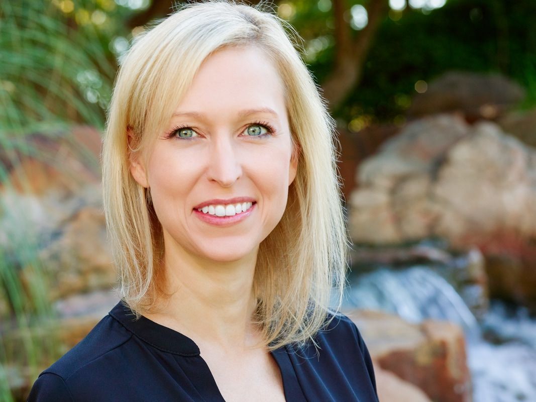 A woman in a black shirt is smiling in front of a waterfall.