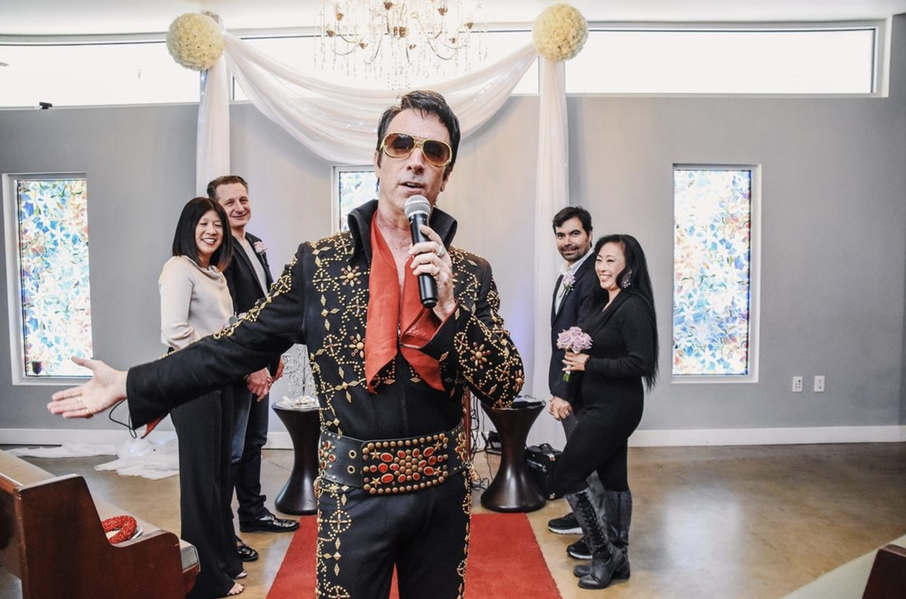 A man in a elvis presley costume is holding a microphone in front of a group of people.