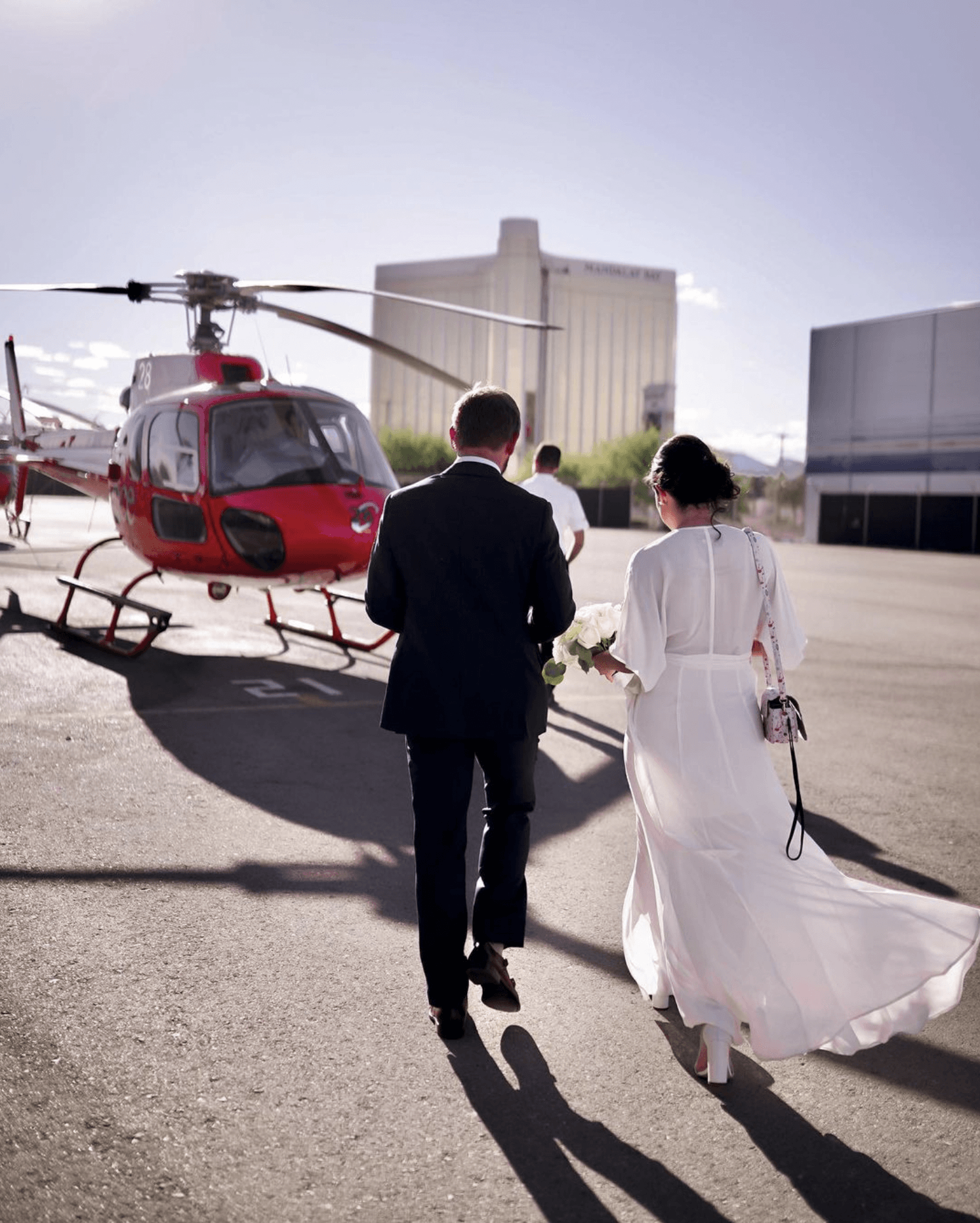 A bride and groom are walking towards a red helicopter.
