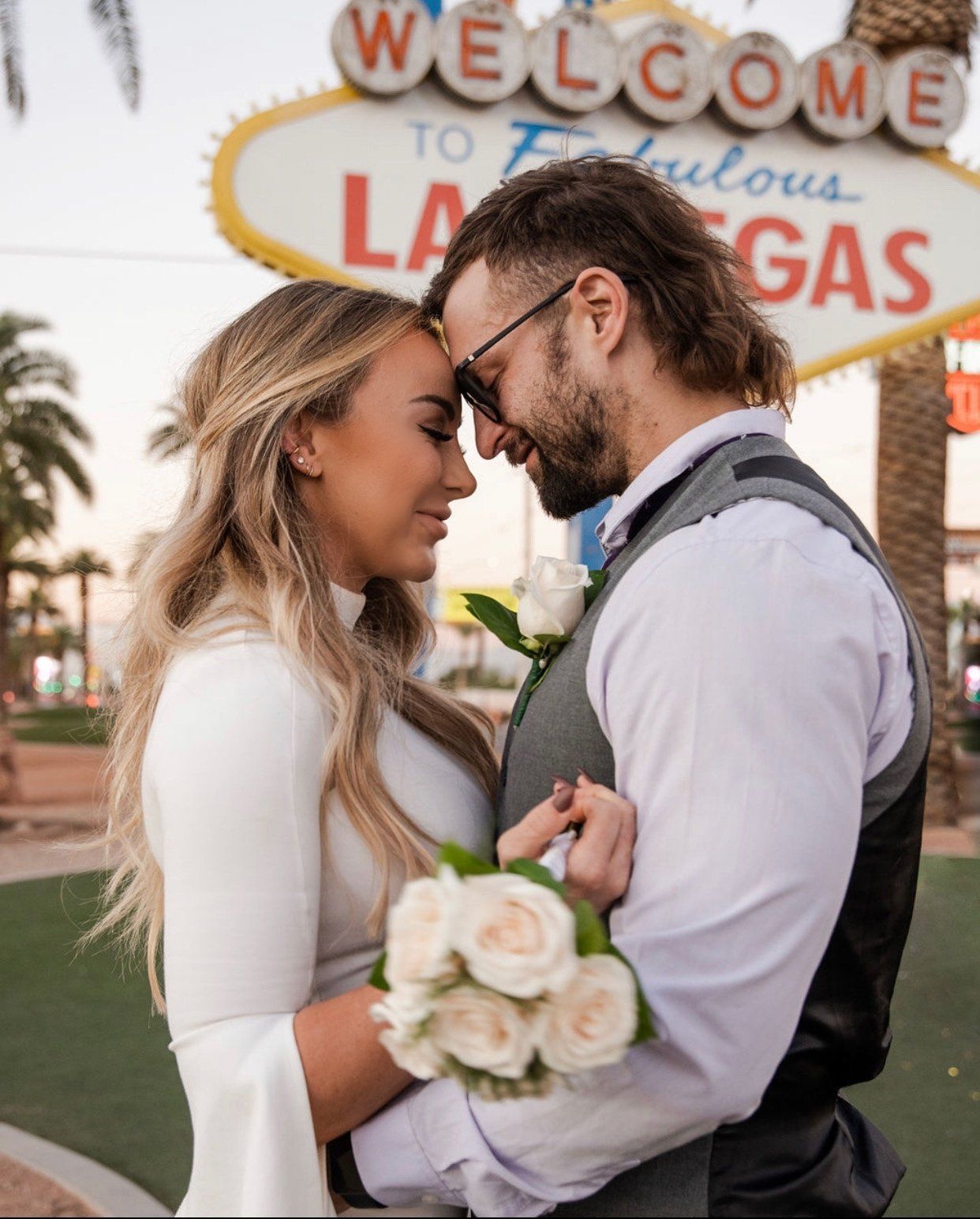 A bride and groom are standing in front of a welcome to fabulous las vegas sign
