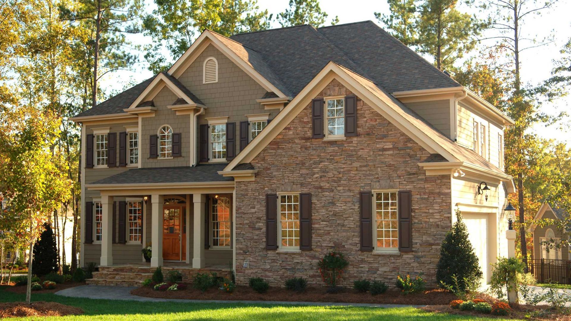 Two-story brick suburban house with tan siding, front porch, and trees in the yard