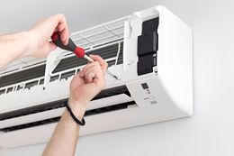 A person is fixing an air conditioner with a screwdriver.