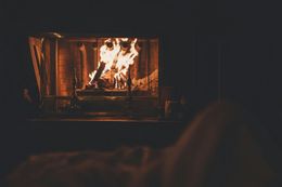 A person is sitting in front of a fireplace with a fire coming out of it.