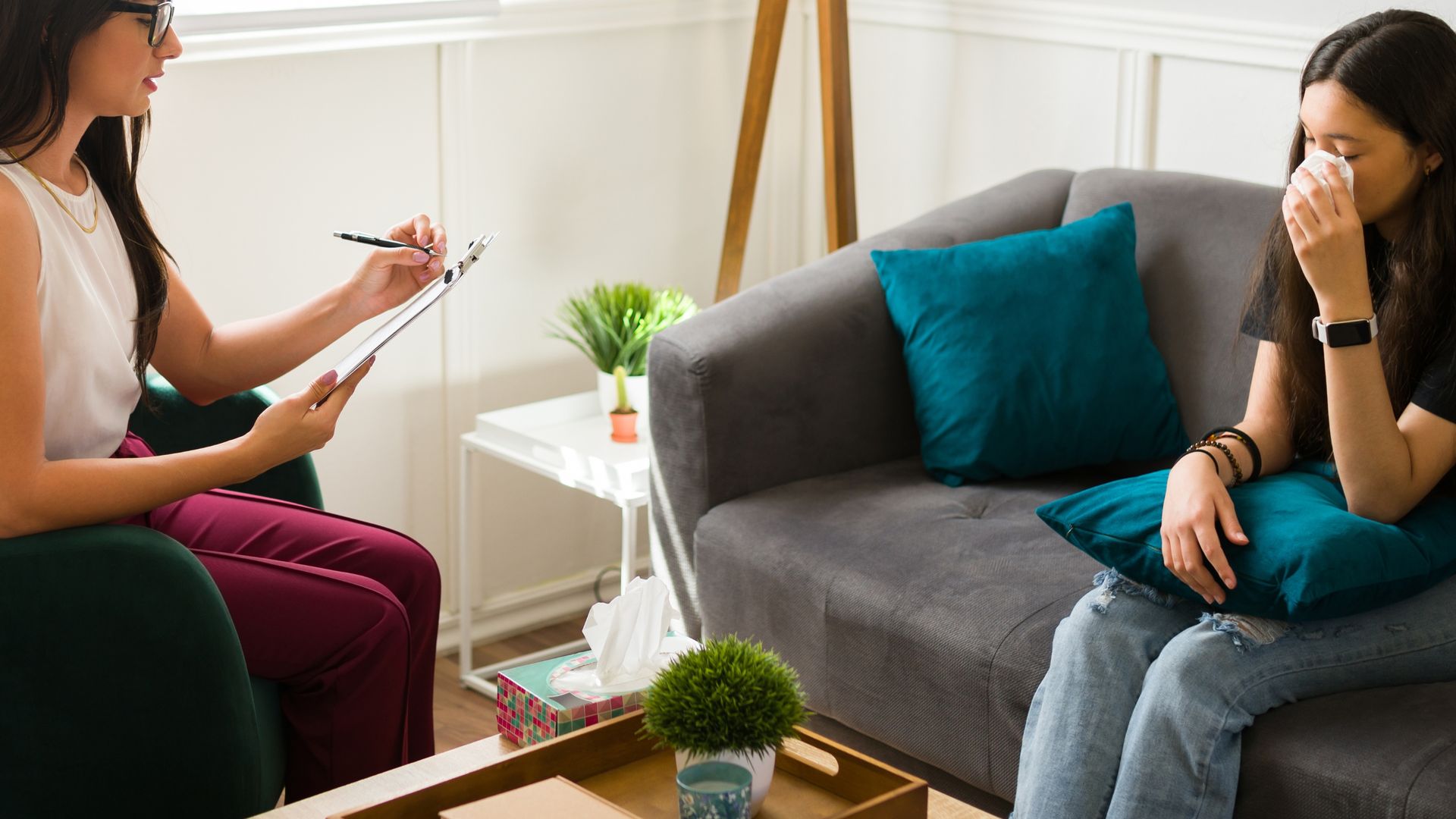 A professional listening to a person crying on a sofa in a therapy office setting.