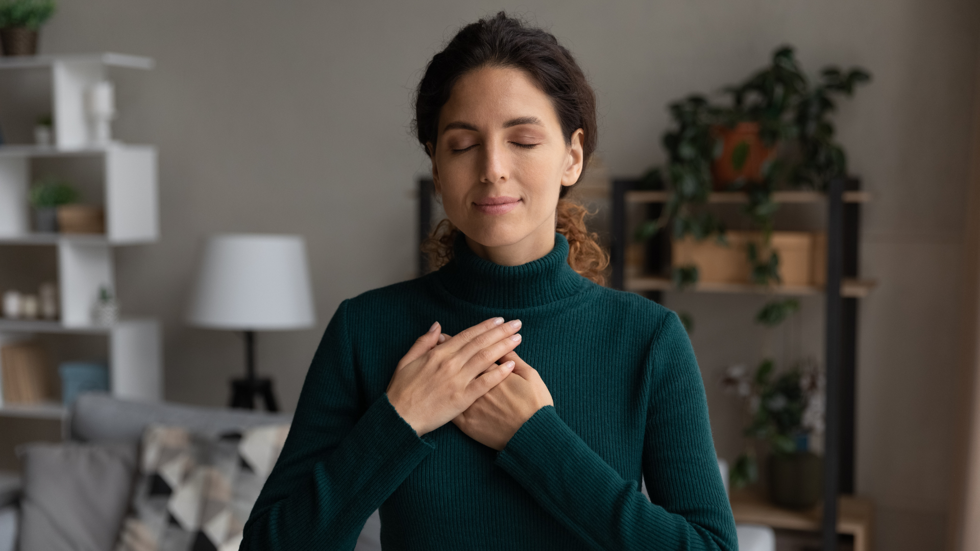 A person sits indoors holding hands with another person, both wearing long-sleeved neutral tops, appearing to be in therapy.