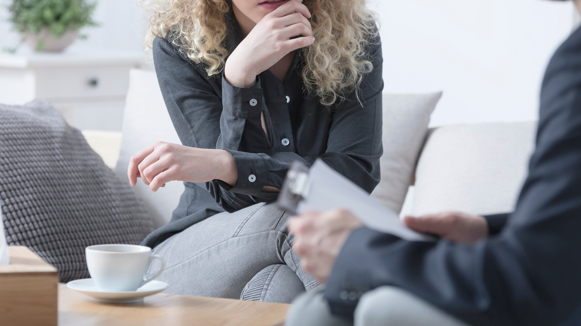 A person in a blue shirt holds the hands of another person, providing comfort and support during a consultation.