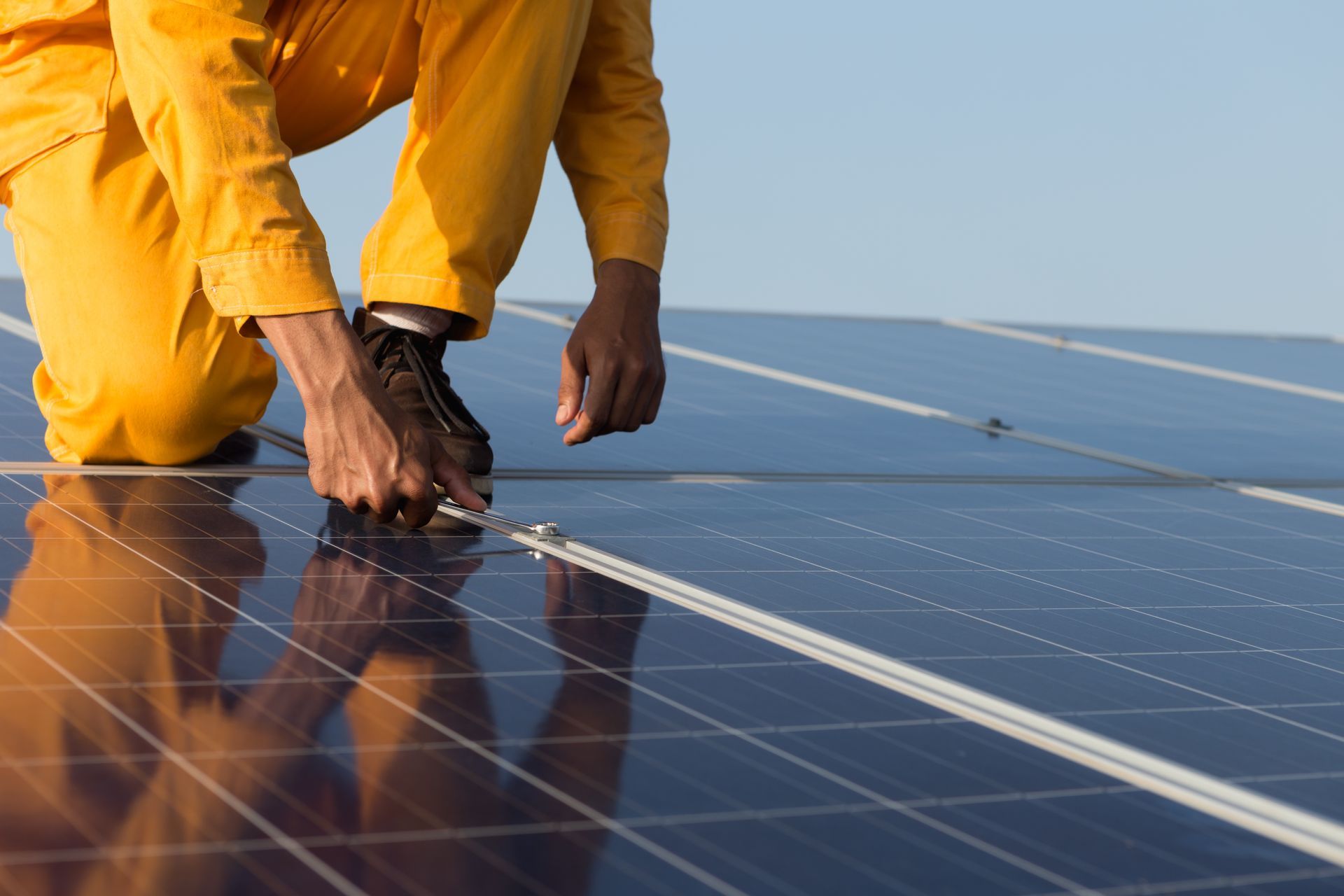 Person in yellow jumpsuit working on solar panels on a rooftop under a clear sky.