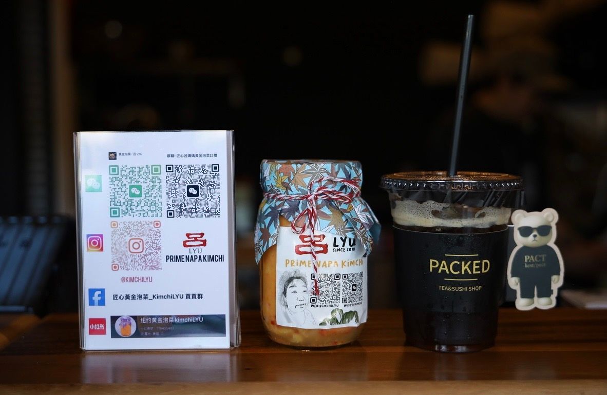 Small display of a QR sign, decorative jar, and black iced drink with straw on a wooden counter.