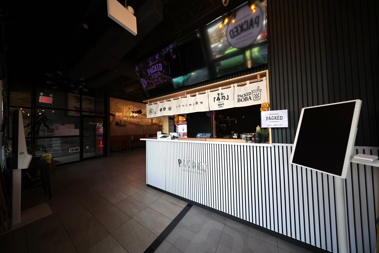 Dim indoor booth with striped counter, menu boards, and a large blank sign in a dark venue.