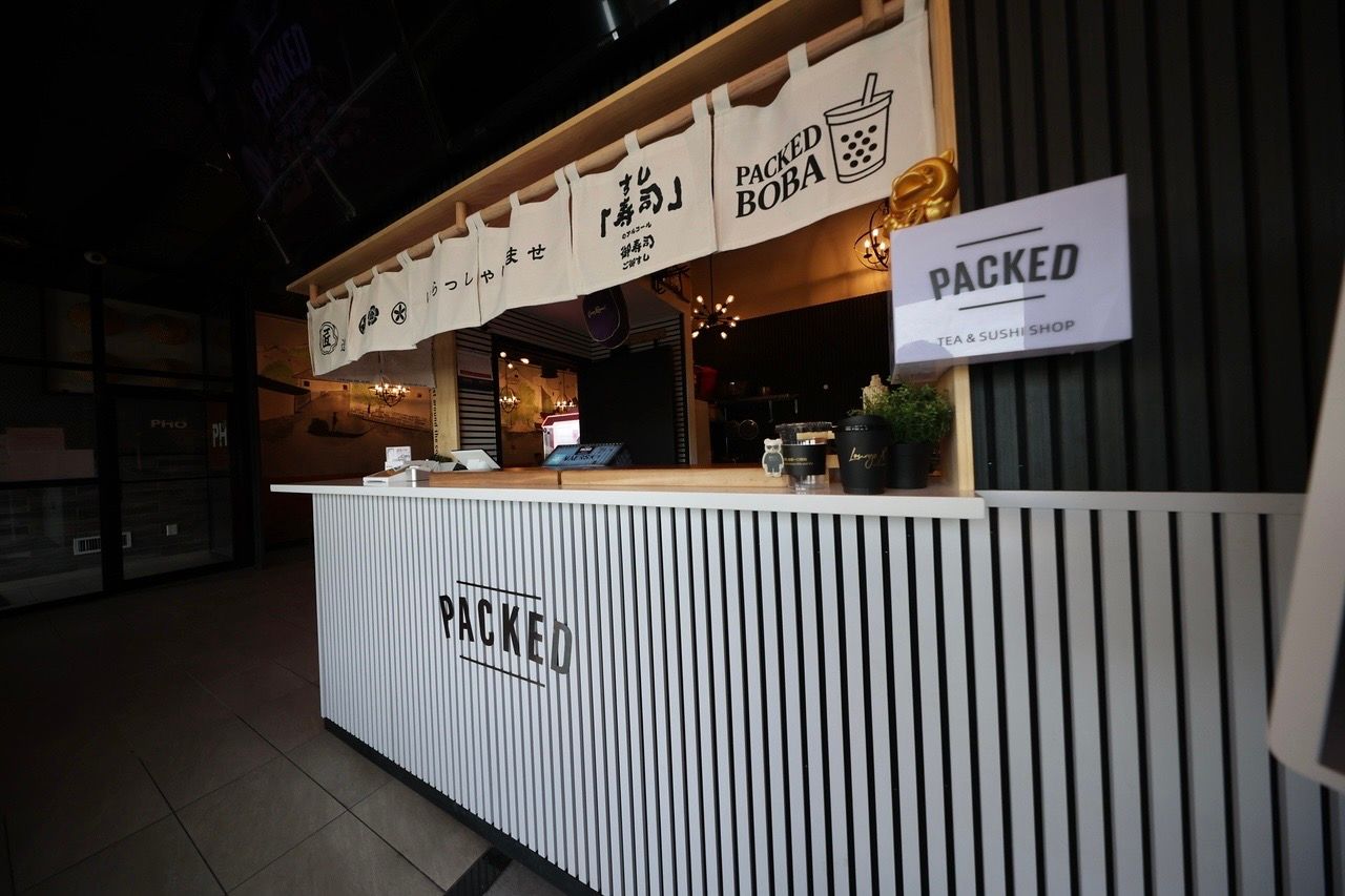 Packed outdoor food stall with striped counter and hanging signs at dusk