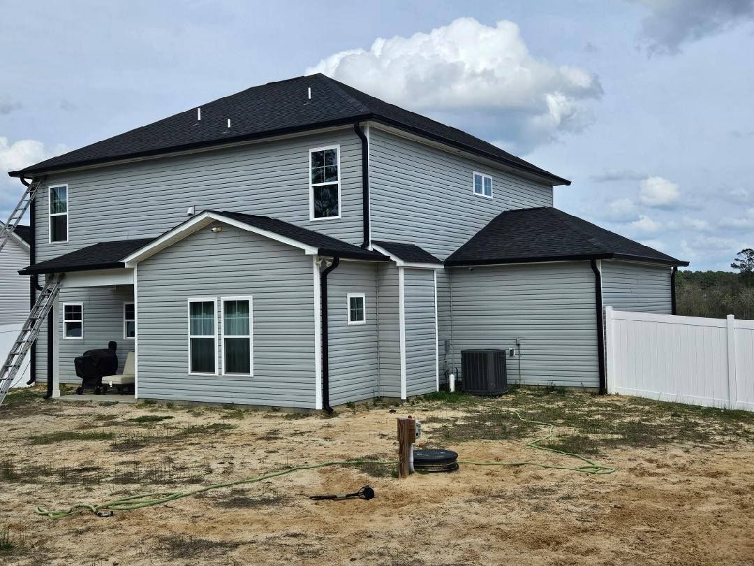A large white house with a black roof is sitting on top of a dirt field.
