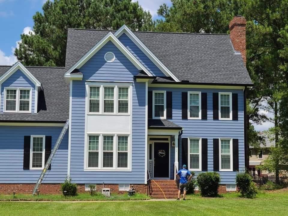A man standing in front of a blue house with black shutters