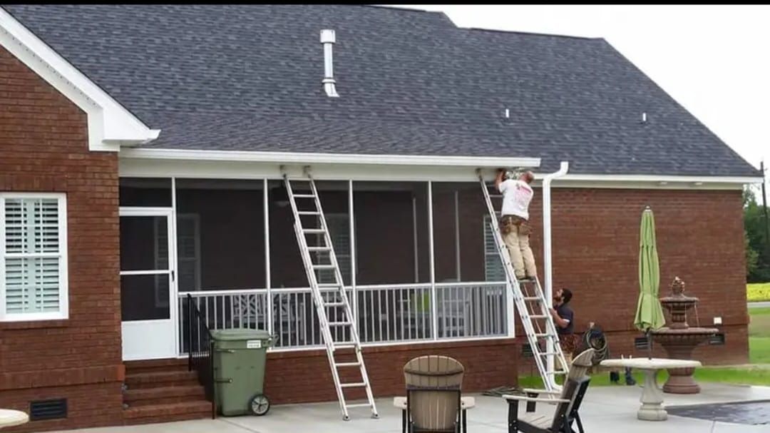 A man is standing on a ladder in front of a screened in porch.