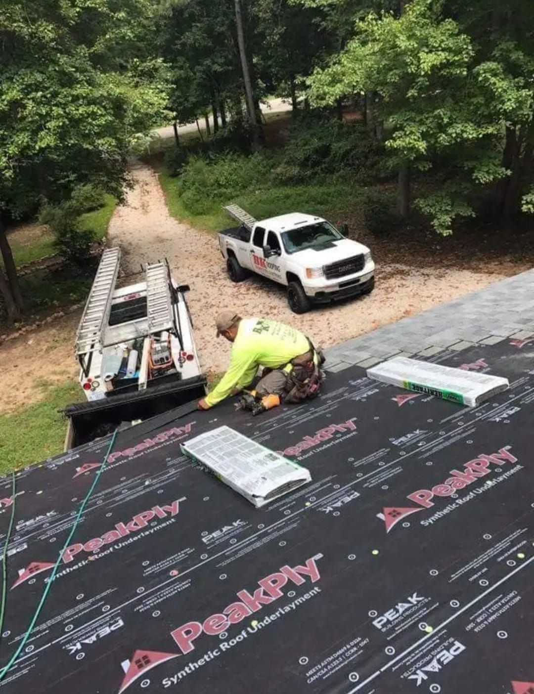 A man is working on a roof with a truck in the background.