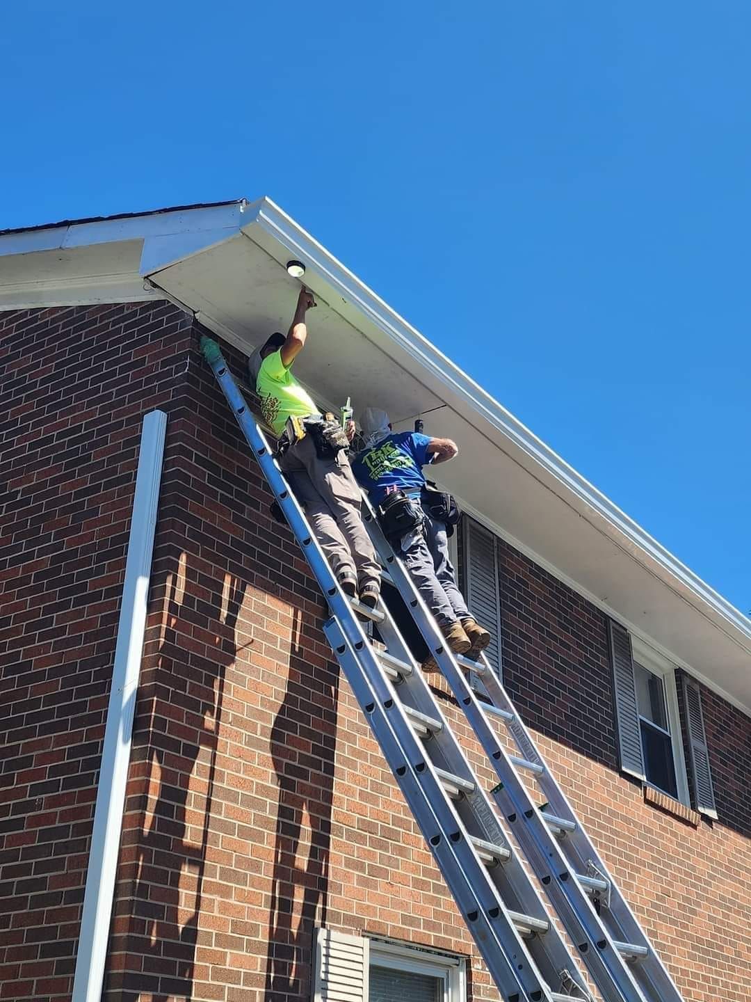 Two men are standing on a ladder on the side of a brick building.