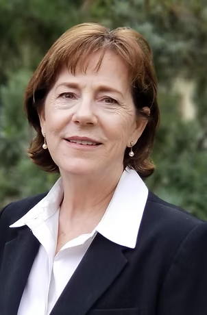 Woman with brown hair in a suit jacket, smiling, outdoors.