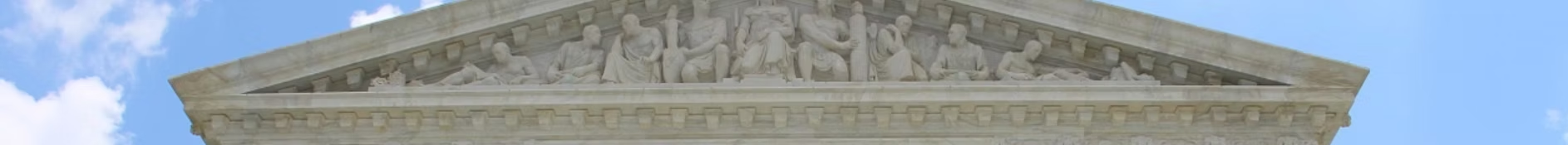 A stone building with a triangular pediment against a blue sky with clouds.