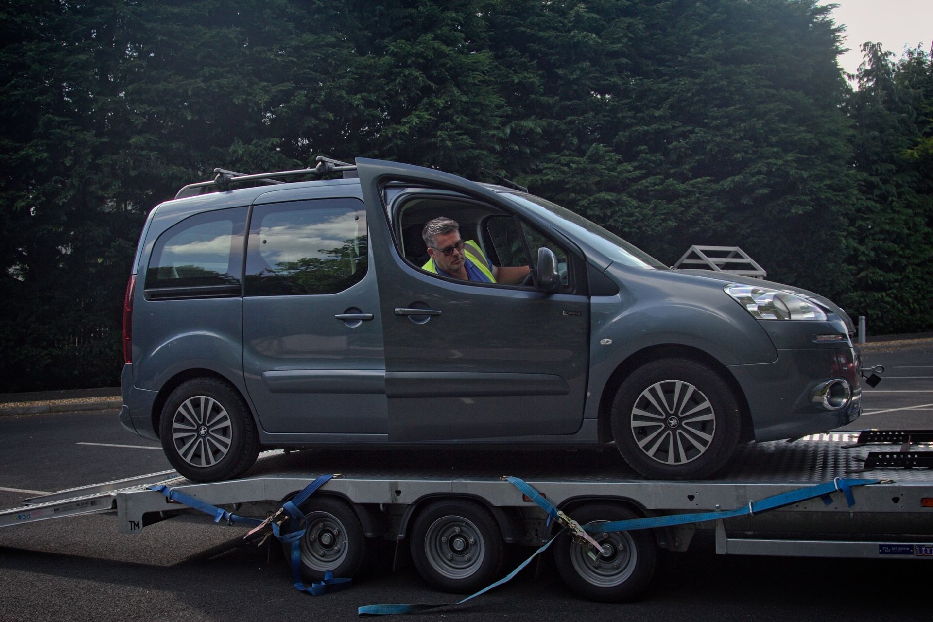 A man is loading a broken down car onto a 24hr recovery trailer.