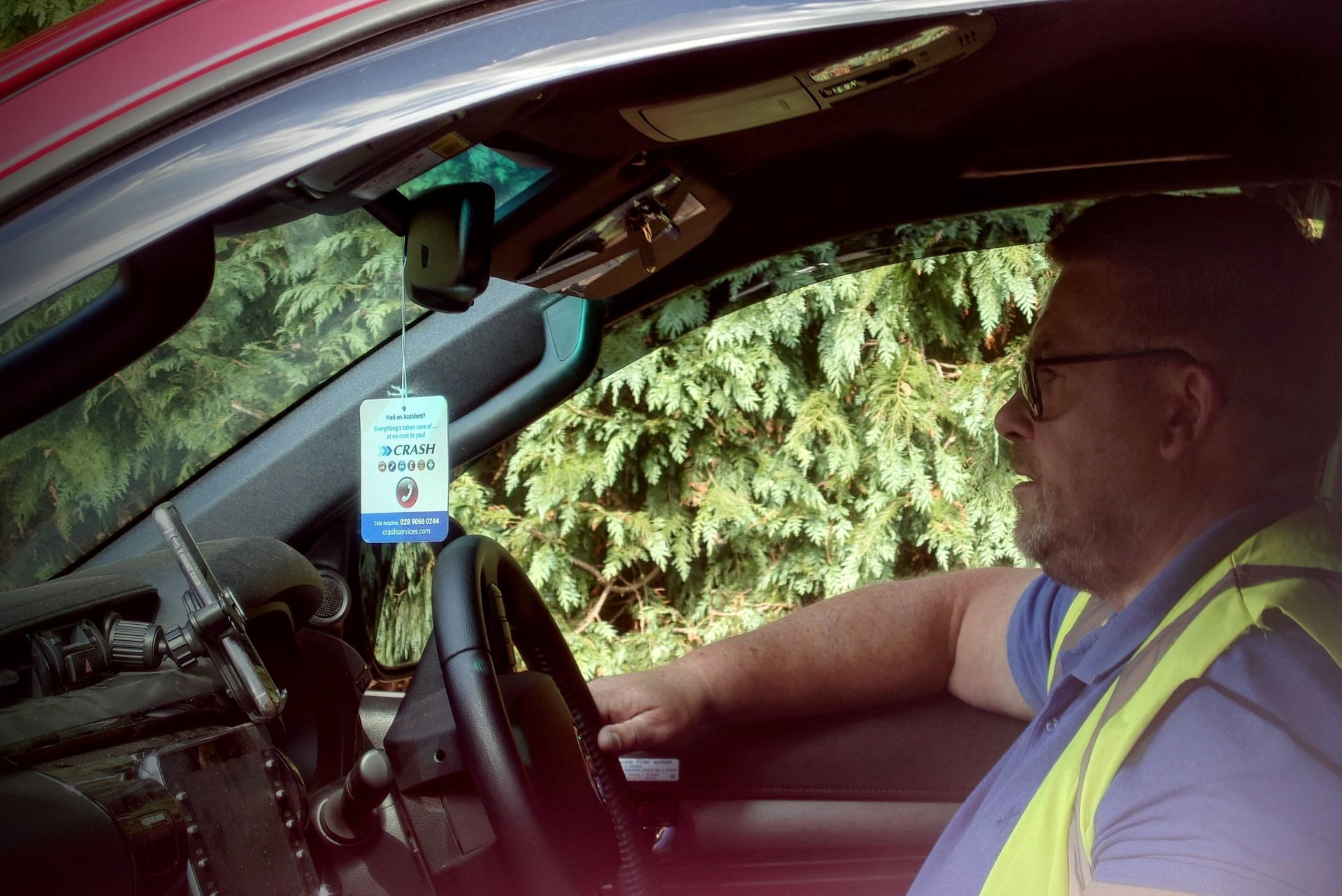 A man in a yellow vest is driving a car.