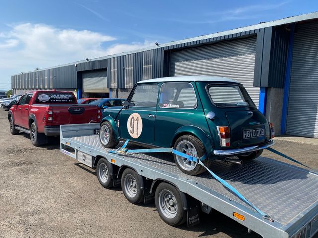 A green mini cooper classic car is sitting on top of a vehicle transportation trailer being transported from Ballymarlagh County Antrim.