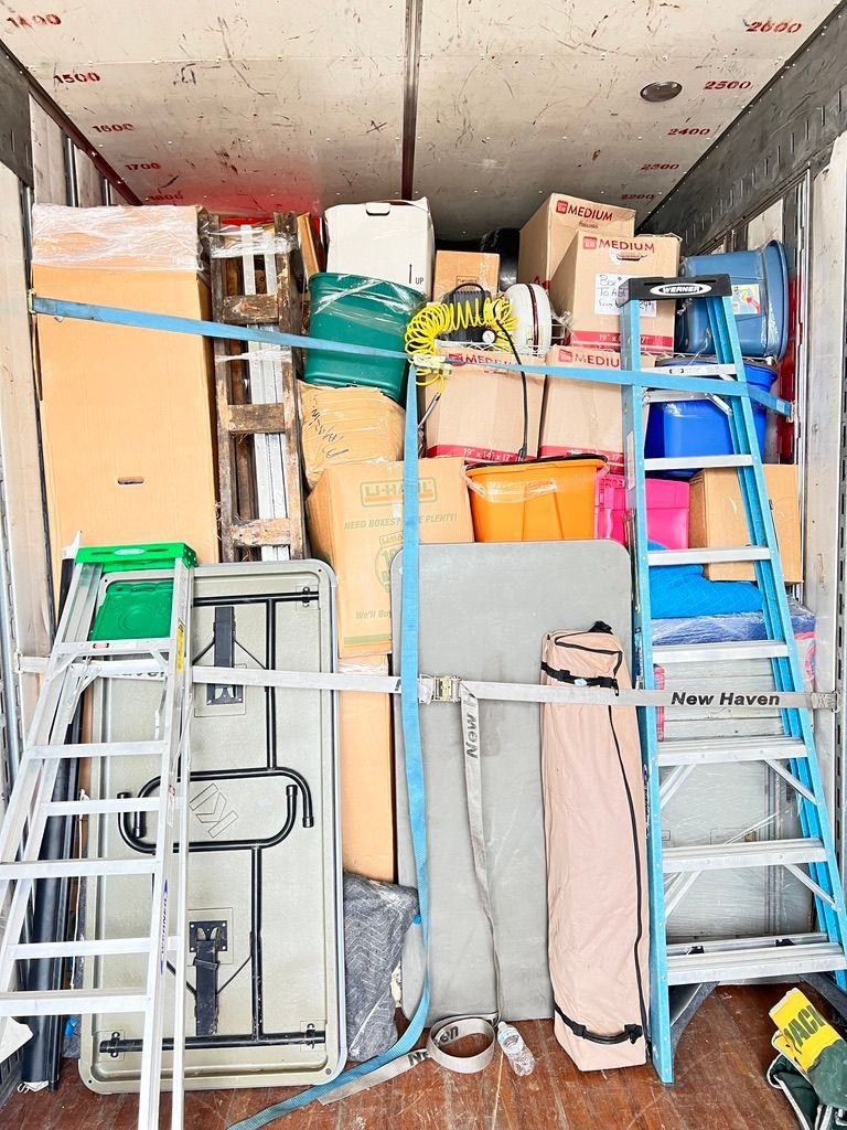 A moving truck filled with boxes , tables , ladders and other items.