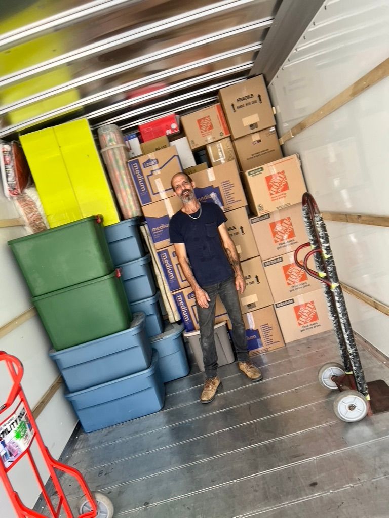 A man is standing in the back of a moving truck filled with boxes.