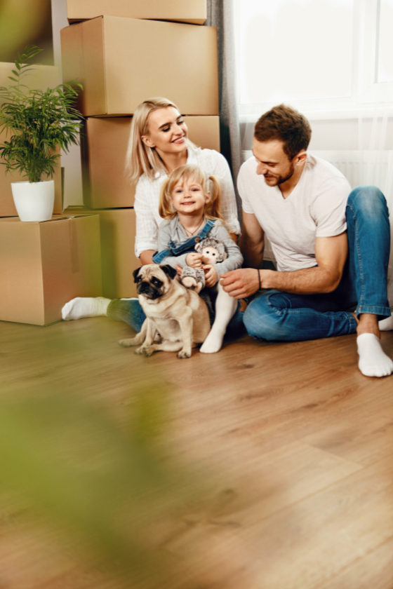 A family is sitting on the floor with their dog in a new home.