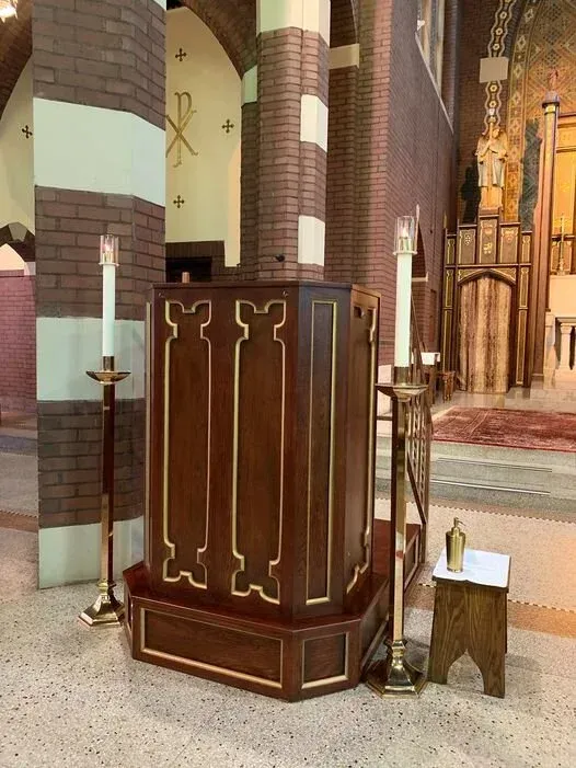 Wooden church pulpit with ornate gold trim beside brick columns and altar candles