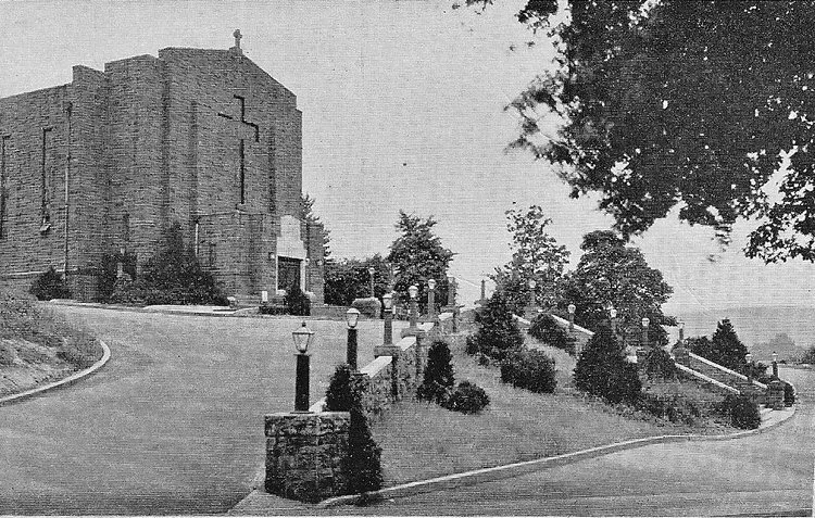 Black-and-white view of a large stone building beside a curved driveway and landscaped shrubs under trees