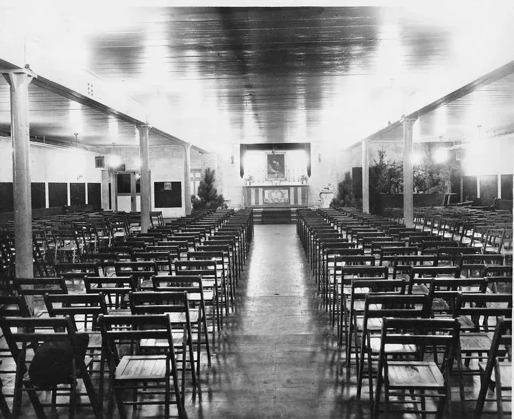 Empty church interior with rows of pews leading to an altar, in black and white.