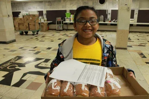 Smiling child holding a box of loaves in a tiled hall