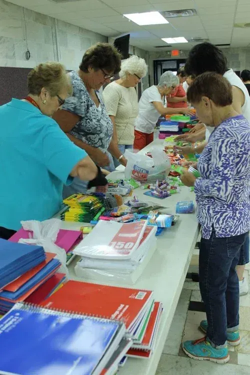 People browsing colorful stationery items on tables at a community sale indoors