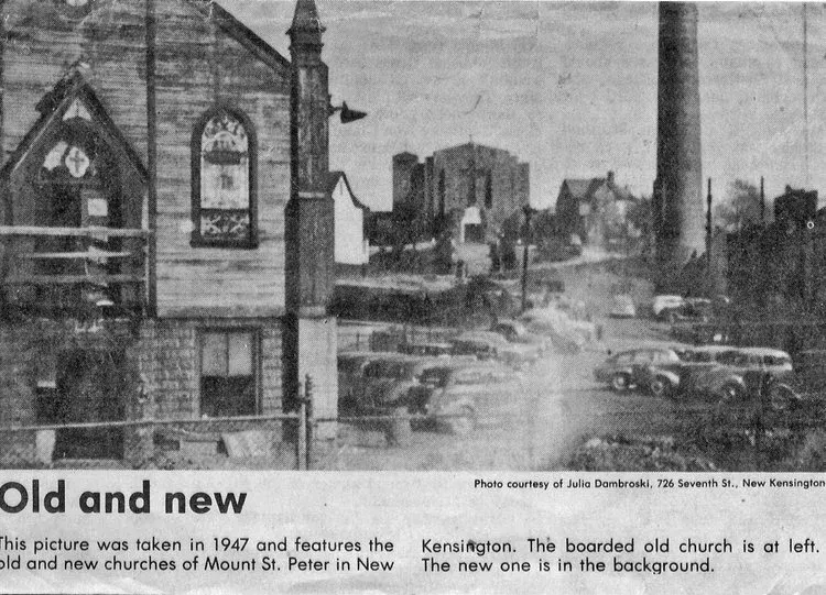 Black-and-white city street scene with old houses, parked cars, and smokestacks in the distance