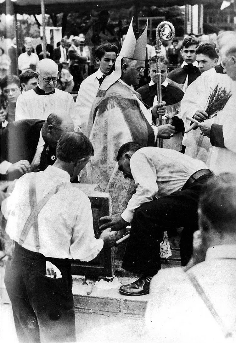 Historical black-and-white crowd gathered around a seated figure at an outdoor ceremony