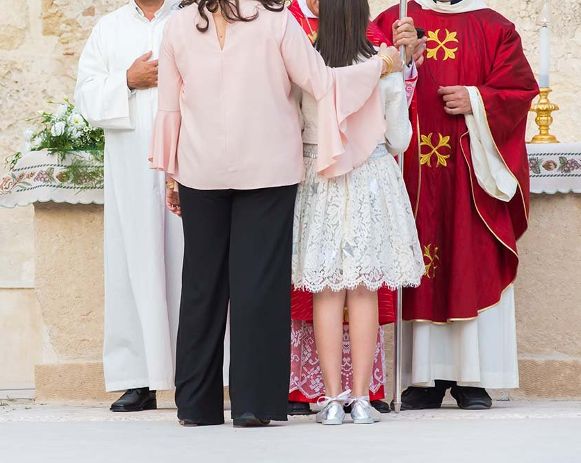 People standing in ceremonial robes, with a child in a white dress at the center.