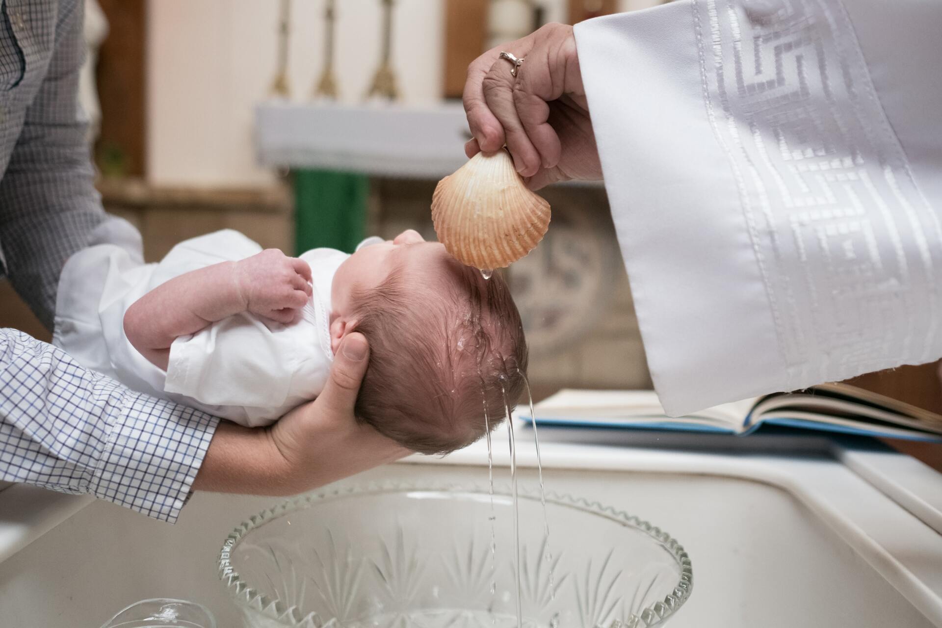 Baby being baptized with water in a church, held over a baptismal font by a priest.