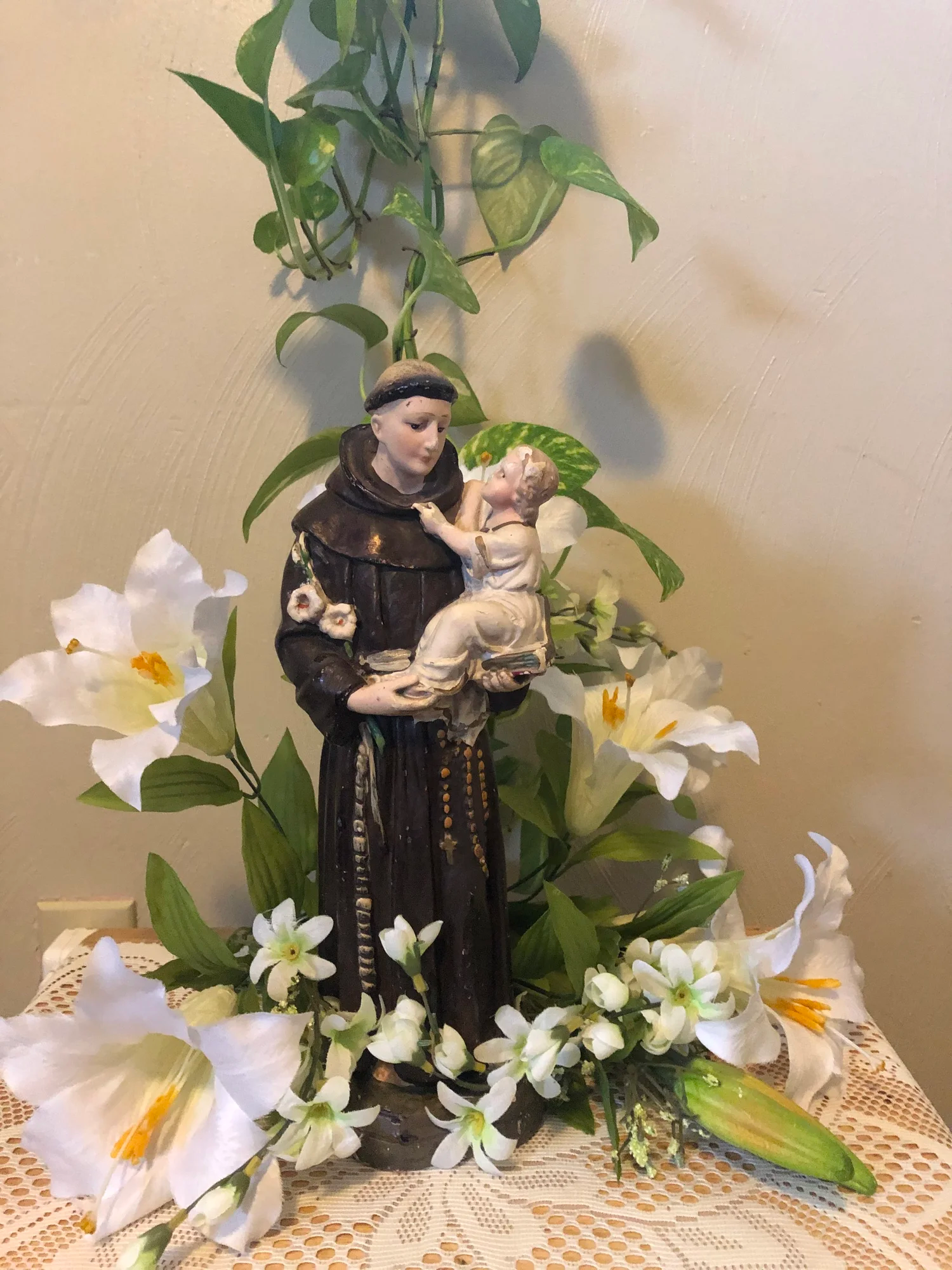 Saint Francis statue holding baby Jesus, surrounded by white flowers and green vines