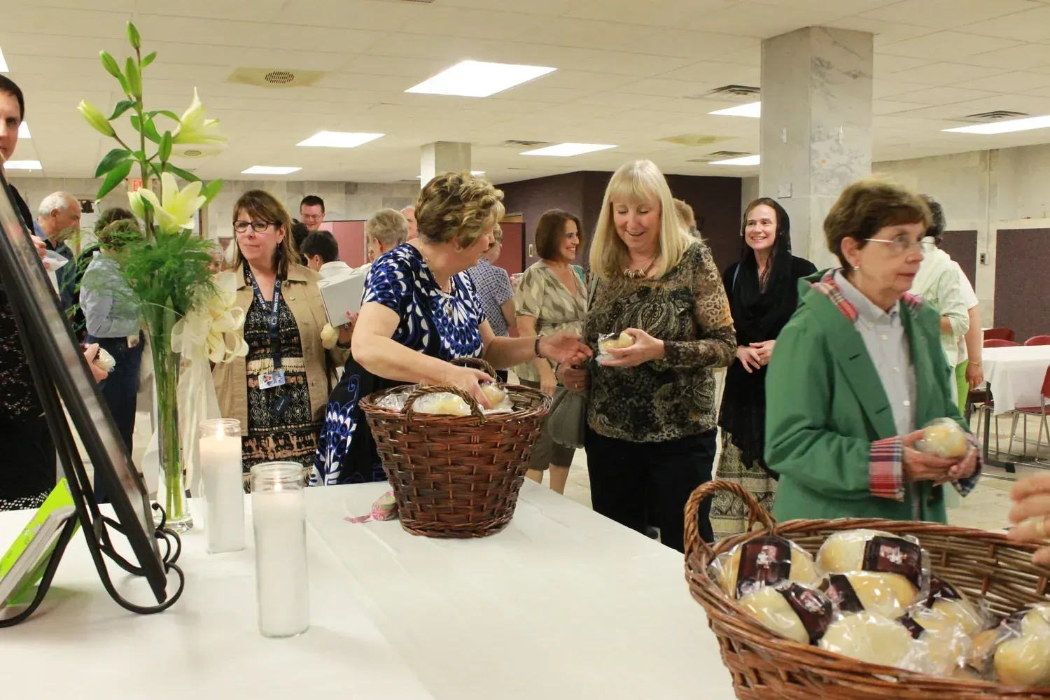 People browsing baked goods at a table in a community hall.