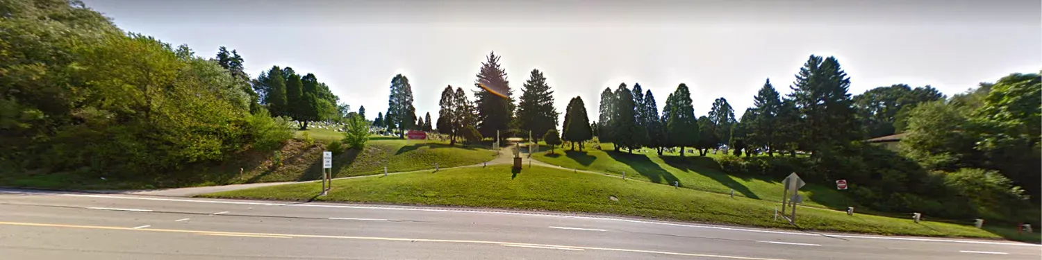 Wide green park with a grassy hill, trees, and a winding path under a bright sky