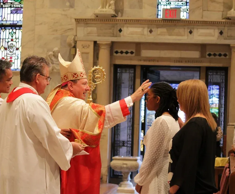 Priest in red robes blessing two people inside a church during a ceremony